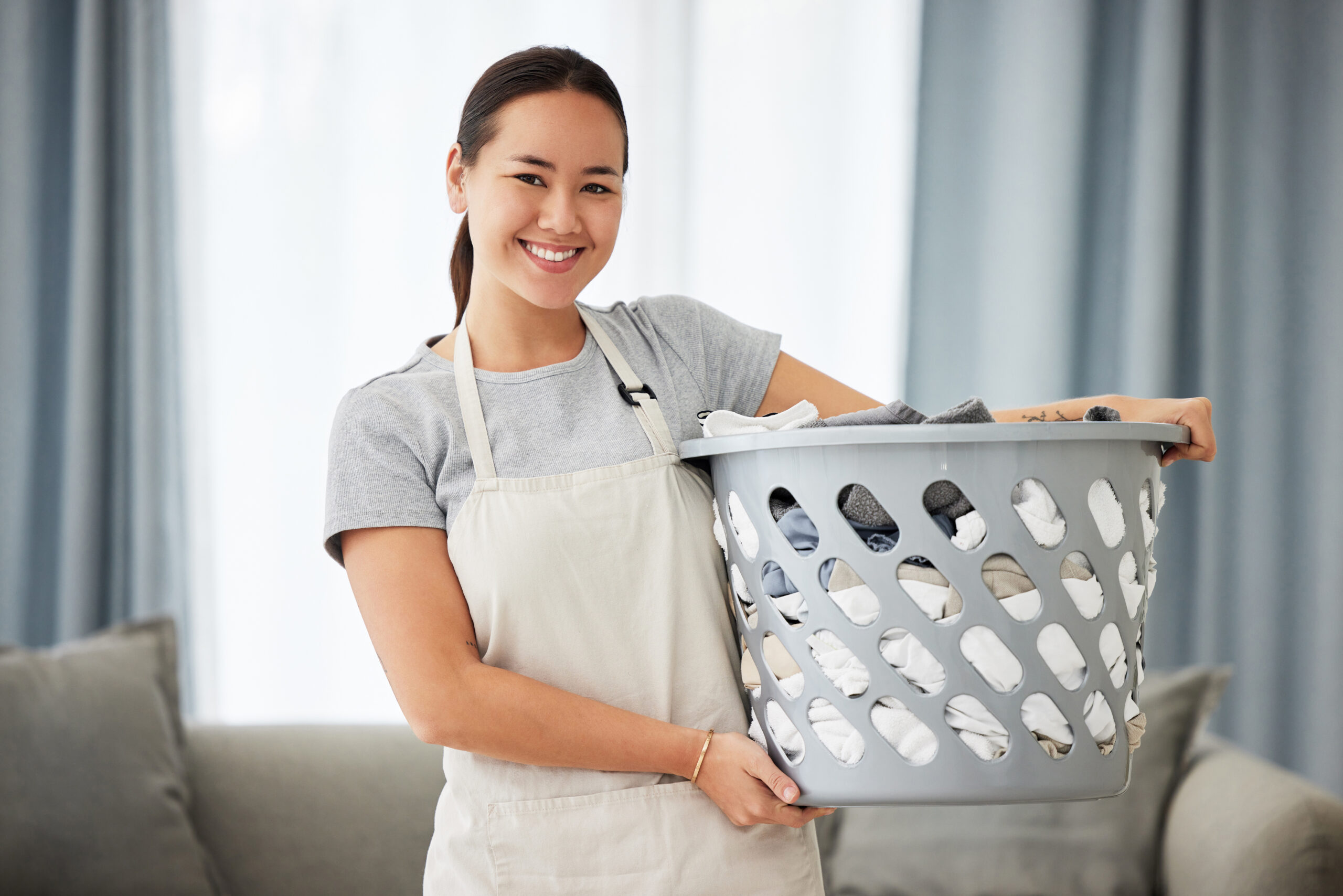 Portrait, home and woman with a laundry basket, smile and cleaning with chores, housekeeping and maid. Face, female person and cleaner with dirty clothes, apartment and washing fabric with service.